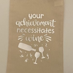 Handmade wine bag with the words “Your achievement necessitates wine” in silver, two glasses below the words with a bottle pouring above the glasses.